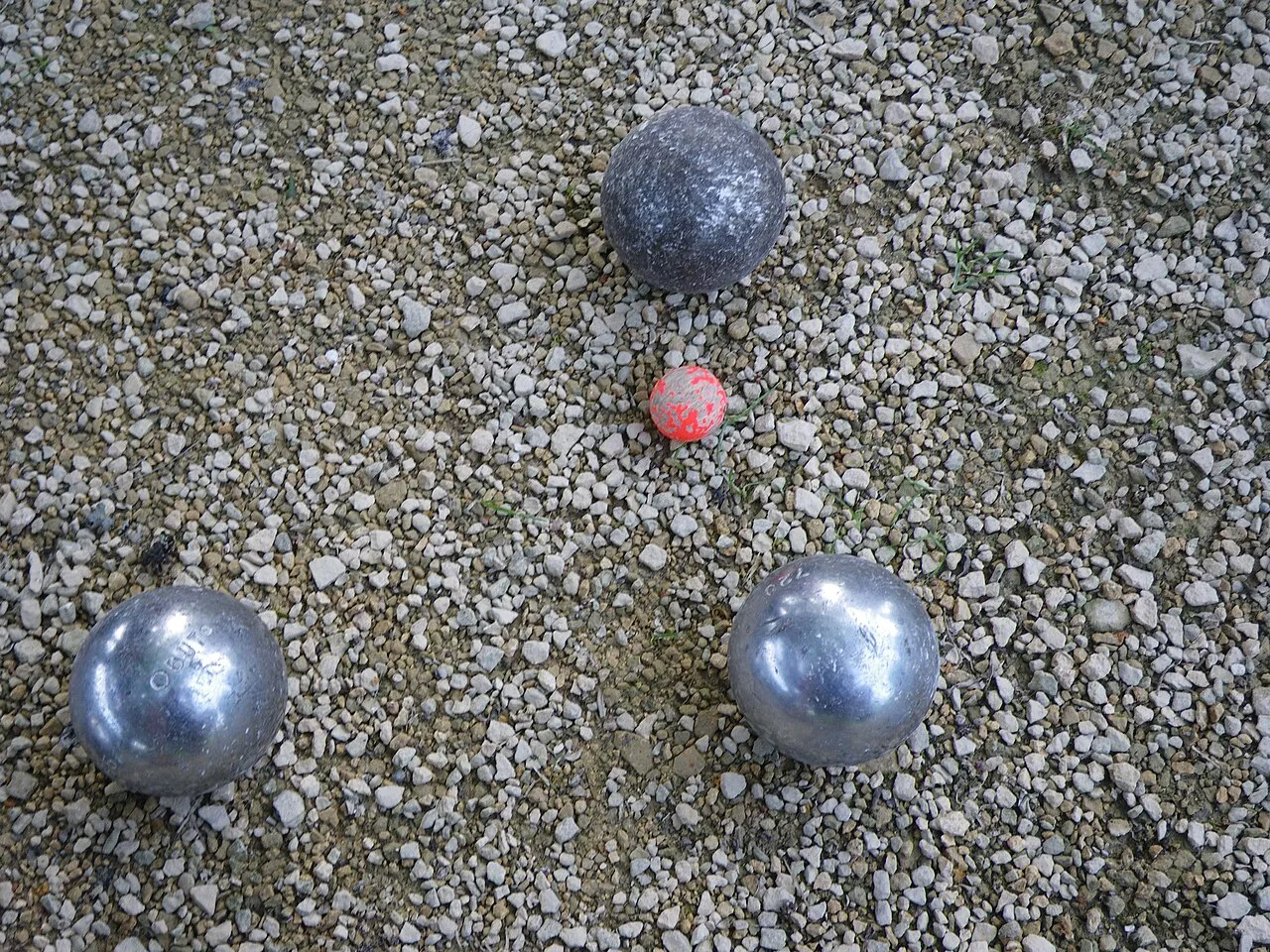 Drie petanqueballen rond een but op grind