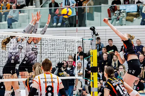 Joueuses de volley-ball disputant un point au filet dans un gymnase